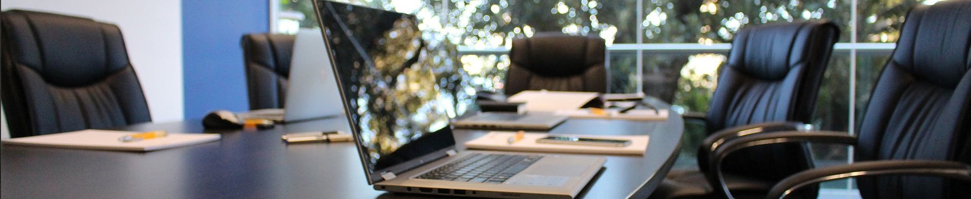 A photo of a meeting room with laptops and notebooks neatly arranged on a table, surrounded by chairs.
