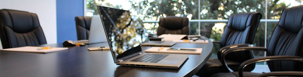 A photo of a meeting room with laptops and notebooks neatly arranged on a table, surrounded by chairs.