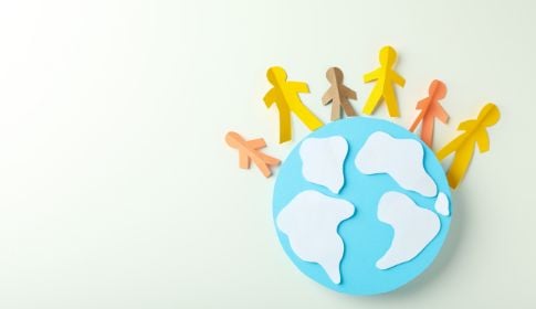 A paper cutout of a globe with small hand-holding figures of different height and colour arranged halfway around its circumference.