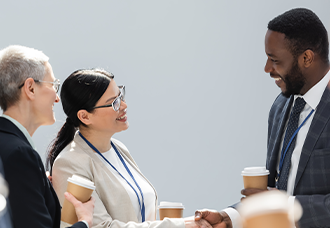 An Asian woman shaking hands with an African man at a conference, both holding a beverage in their hands.