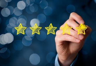 An image of a person's hand drawing five yellow stars against a dark, glittery background.