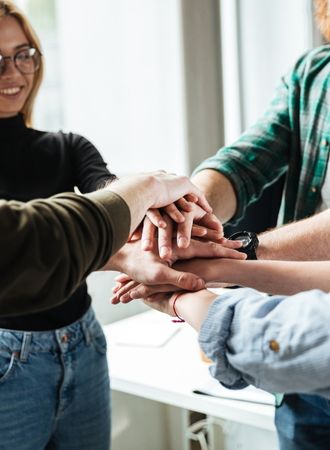 A photo of people placing their hands on top of each other's hands to show solidarity.
