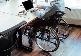 A person in a wheelchair sitting at a desk and typing on a laptop.