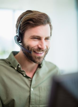 A Caucasian man wearing a headset, laughing and looking at his laptop.