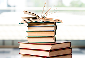 Books are stacked on top of each other with the top book open with some pages in mid air.