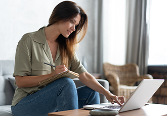 A photo of a female student referencing something on her laptop while reviewing her notes.
