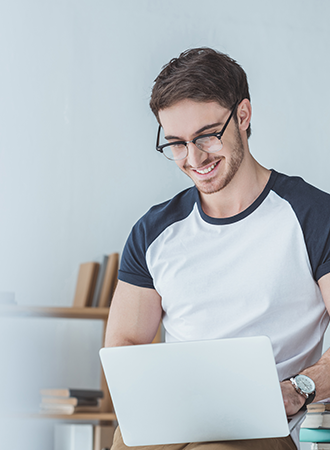 Opportunities An Caucasian man wearing a t-shirt and glasses, smiling while working on his laptop.