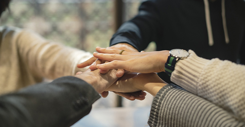 A photo of people placing their hands on top of each other to show solidarity.