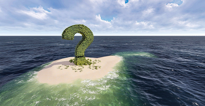 A photo of the sea with a small patch of sand with a tree shaped into a manicured question mark, surrounded by water.