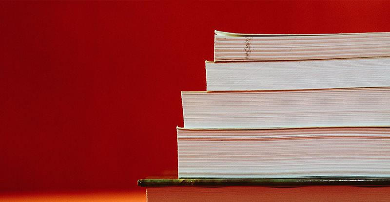 A photo featuring a red background with books arranged on top of each other.