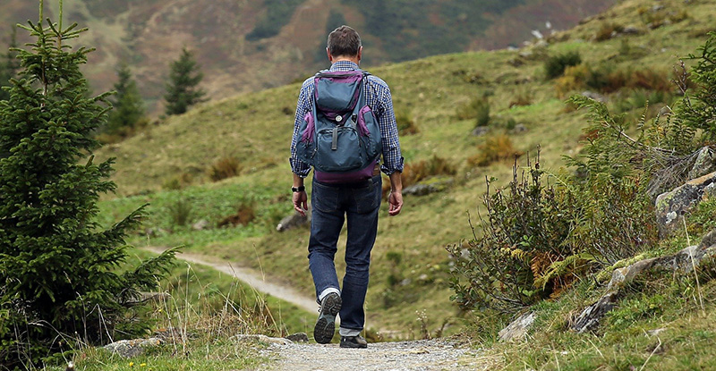 A photo of a man walking with a backpack through a trail.