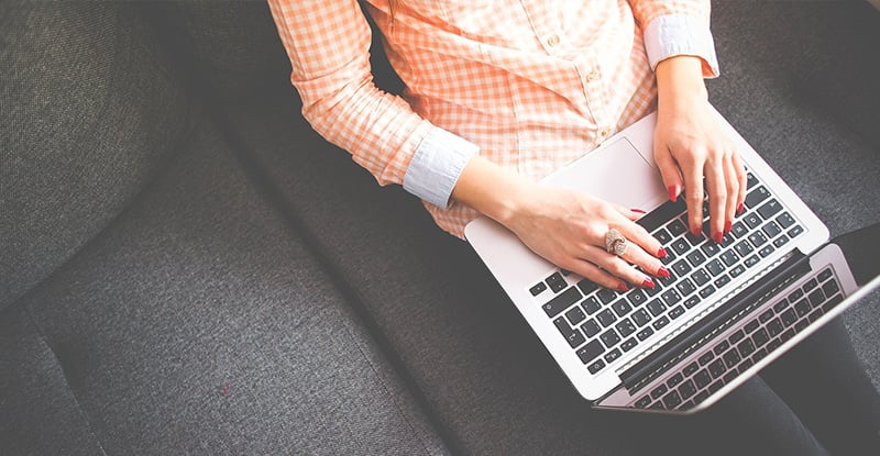 An overhead photo of a woman typing on her laptop while seated on a couch.