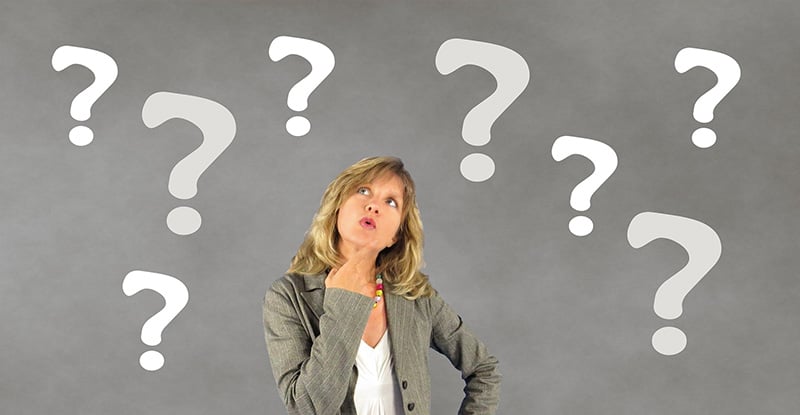 How can I tell if I can write my redesigned course exam? A photo of a woman in a grey suit posing thoughtfully, with white question marks floating around her.