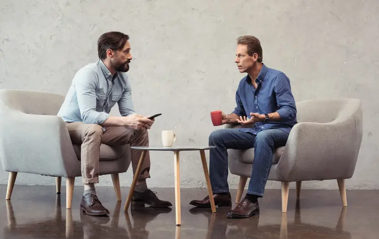 two men sitting in chairs talking to each other