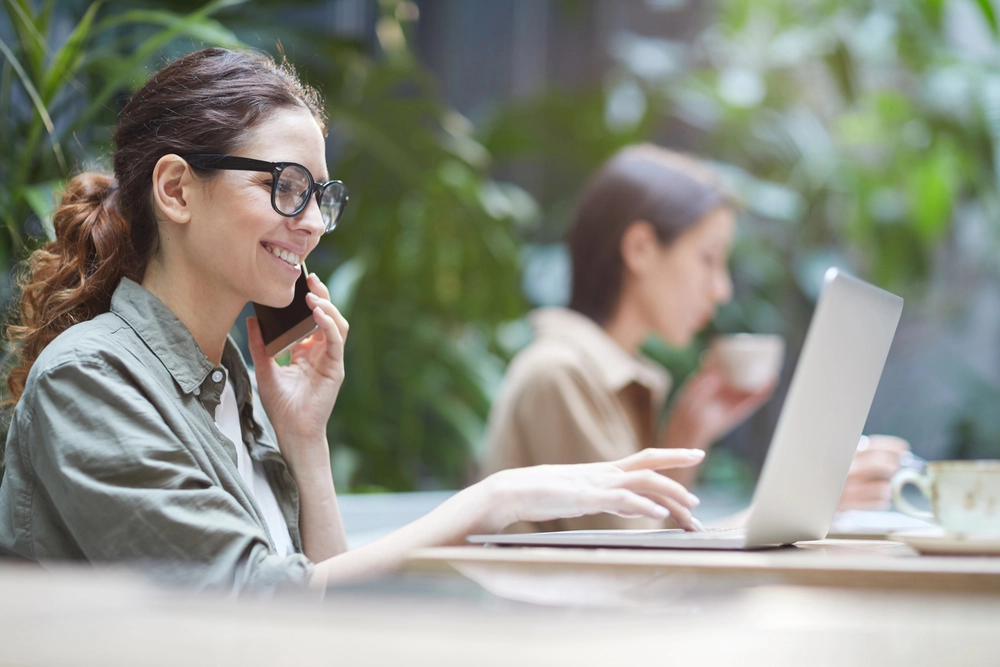 a woman talking on a cell phone while sitting at a table with a laptop