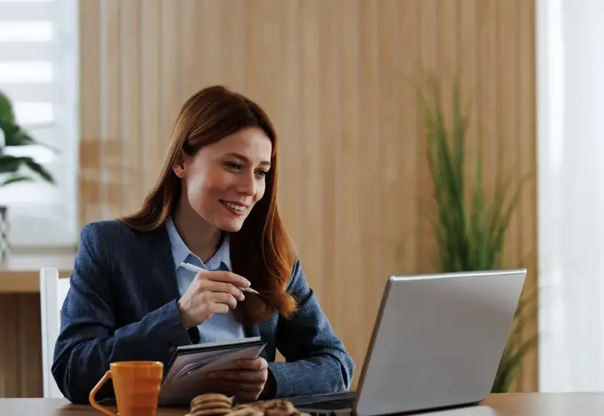 a woman sitting at a desk with a laptop and a pen