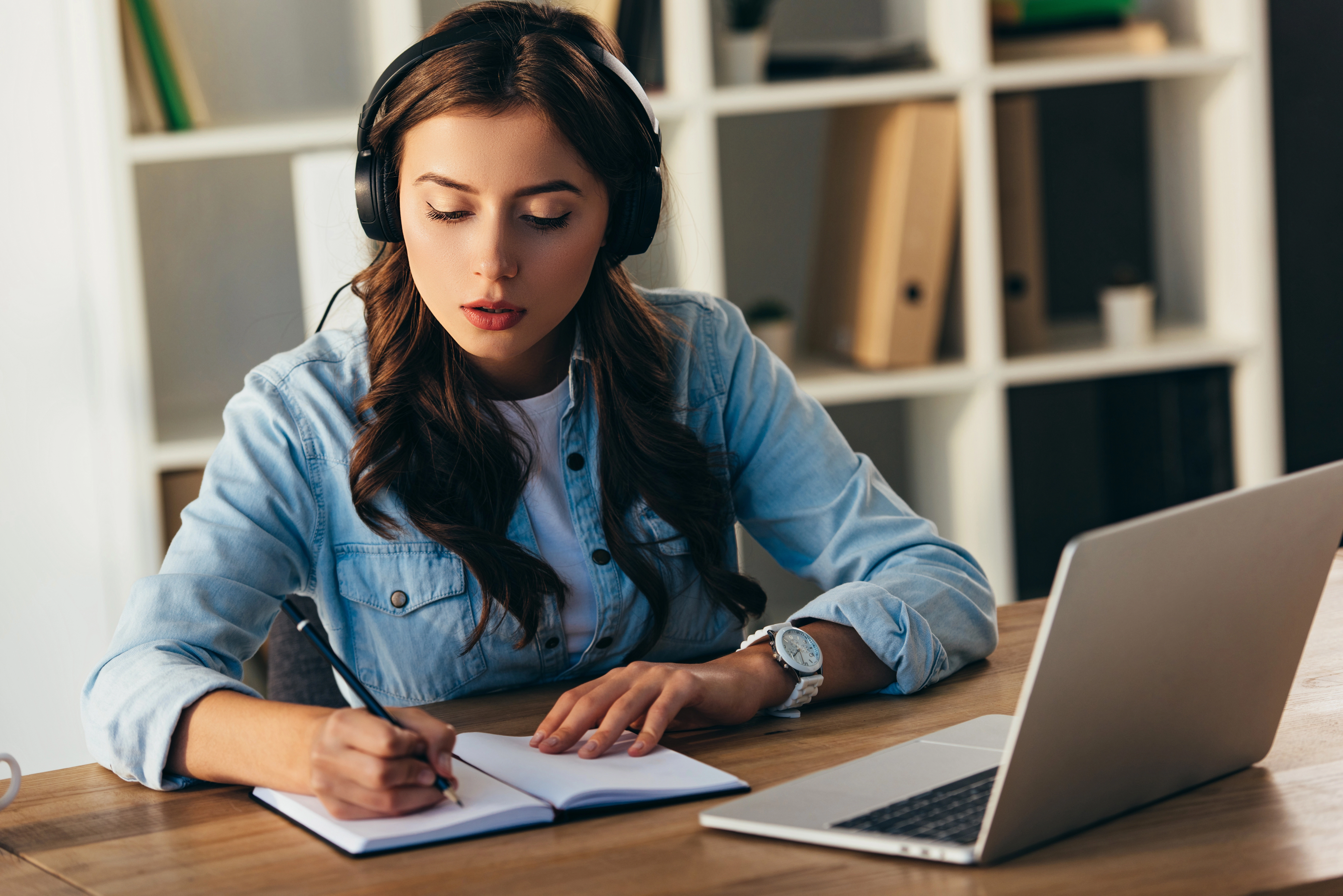 a woman wearing headphones and writing in a notebook