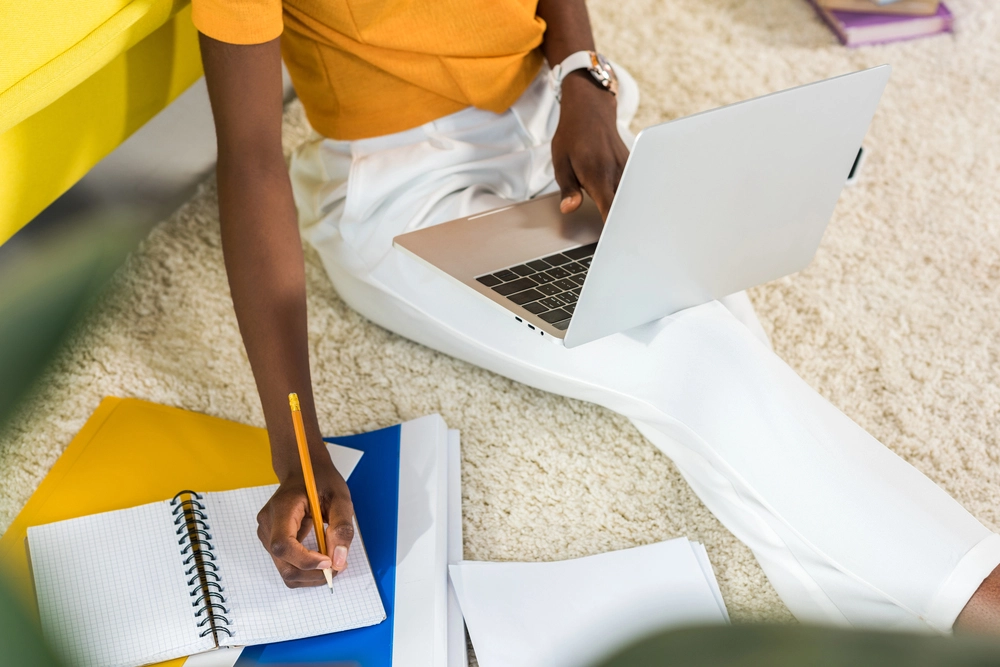 a person sitting on the floor with a laptop and notebook