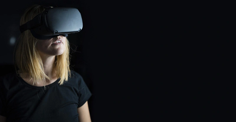 Photo of a woman in a black t-shirt in a VR headset strapped around her head, set on black background.
