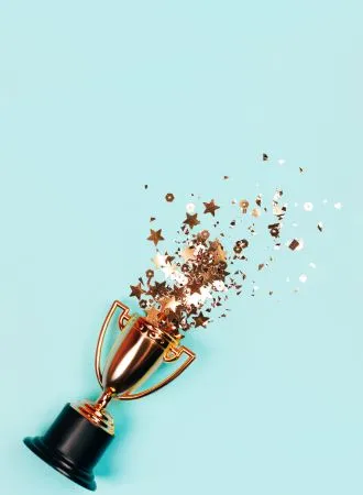 Photo of an award cup with confetti on a plain light blue background.