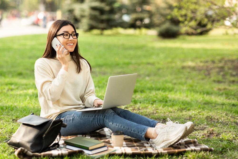 a woman sitting on a blanket with a laptop and phone