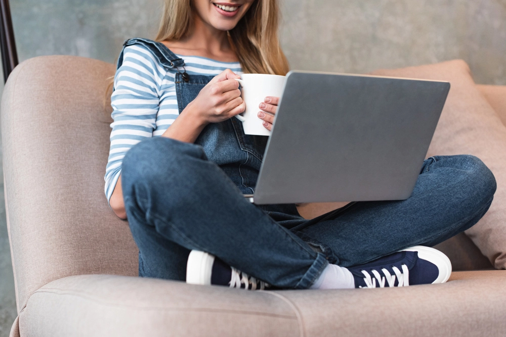 a woman sitting on a couch with a laptop and a cup