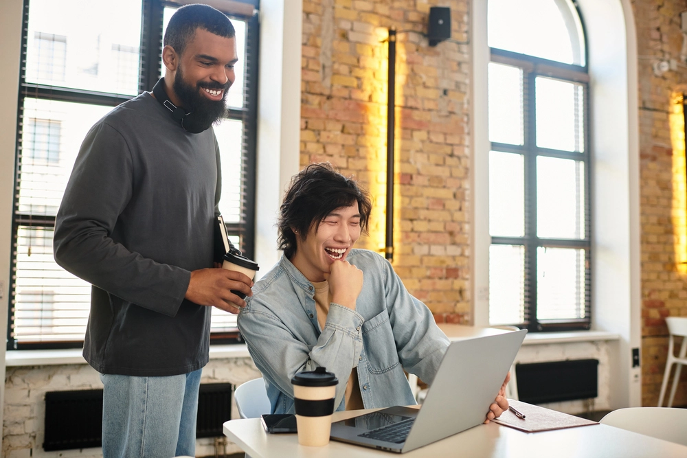 a man standing next to a man smiling at a laptop