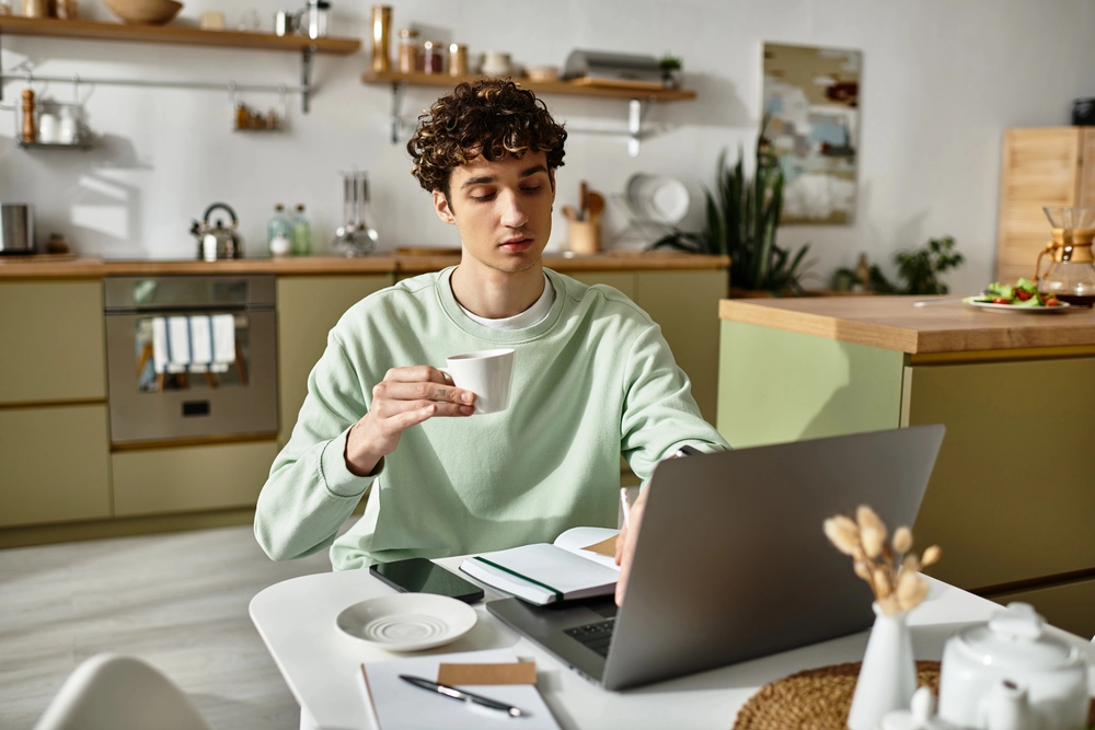 a man holding a cup of coffee and looking at a laptop