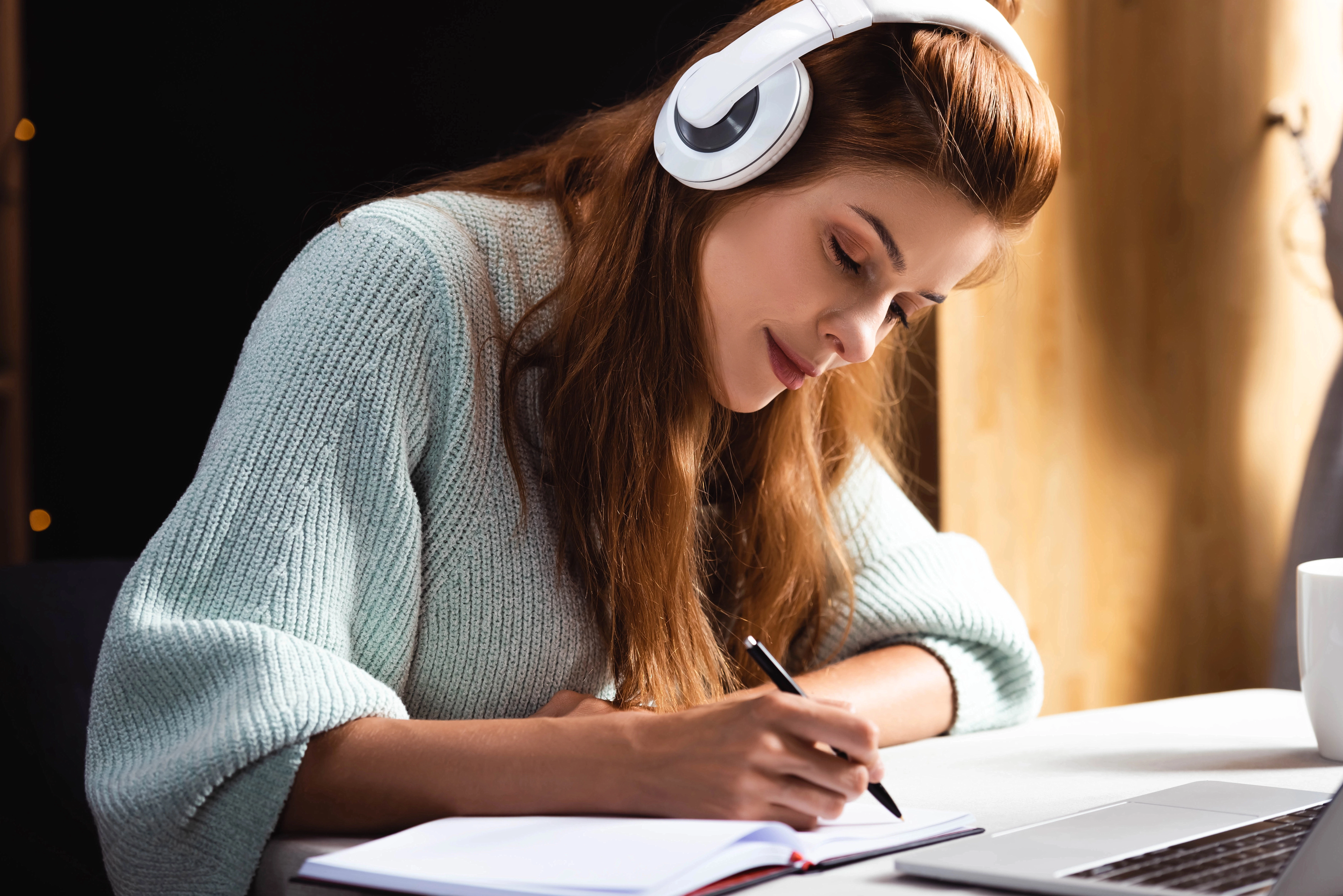 a woman wearing headphones writing on a notebook