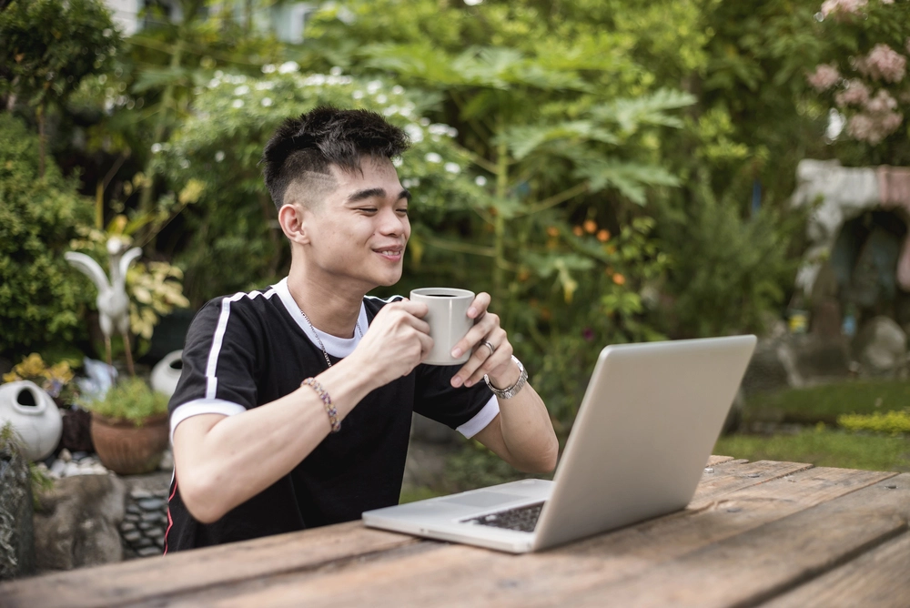 a man holding a cup and looking at a laptop