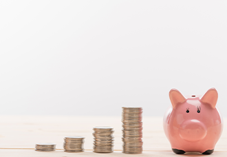 A piggy bank on the right side of the photo with gold coloured coins lined up incrementally toward the pig.