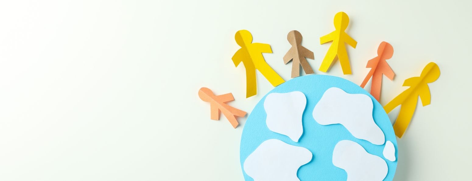 A paper cutout of a globe with small hand-holding figures of different height and colour arranged halfway around its circumference.