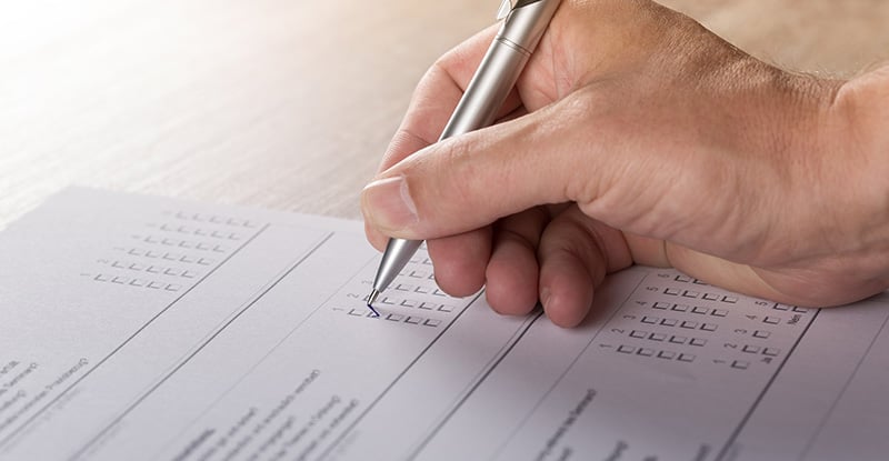 Candidate Survey Feedback: Where does it go? A photo of a person answering multiple choice questions on paper with a black pen.