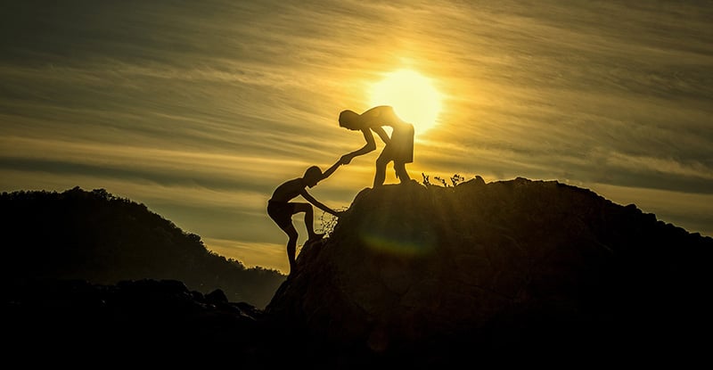 CPA PEP Facilitator Mentor Program A photo of a person giving a hand to another person to climb the top of a mountain.