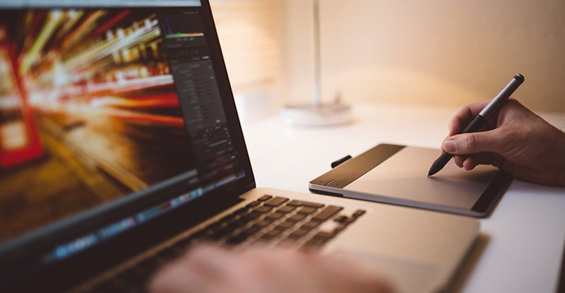 A photo of a person using Adobe photoshop and a design board to draw something.