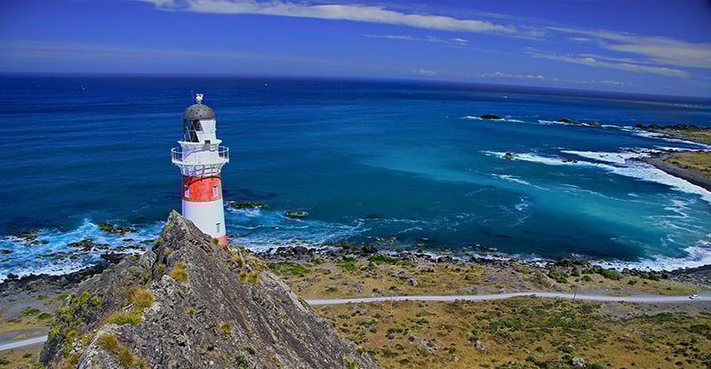 A photo of a beautiful seaside with a lighthouse partially hidden by a mountain.