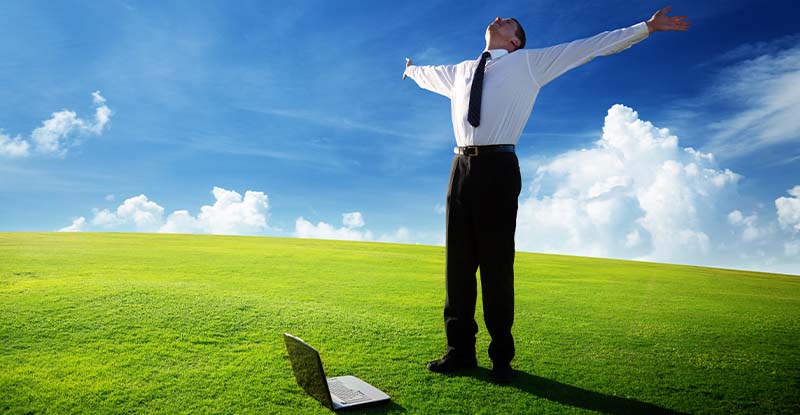 Who’s Your User? Understanding the Importance of Situational Awareness A photo of a man standing with his hands wide open and looking at the sky. There is a laptop on the grass beside his feet to signify freedom.