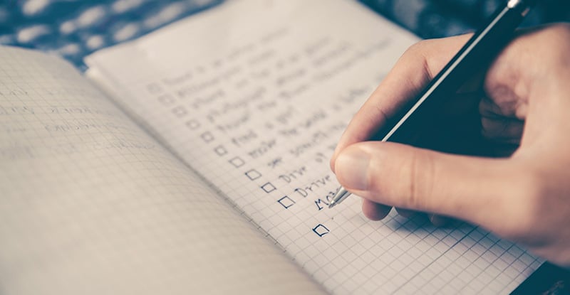 A photo of a notebook where a person is writing a checklist with boxed in front of each points.