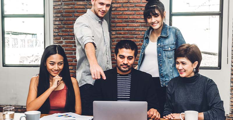 Why should I study with a partner or group when I can study better on my own? A photo of a group of students working together on one laptop with one student pointing at the laptop.