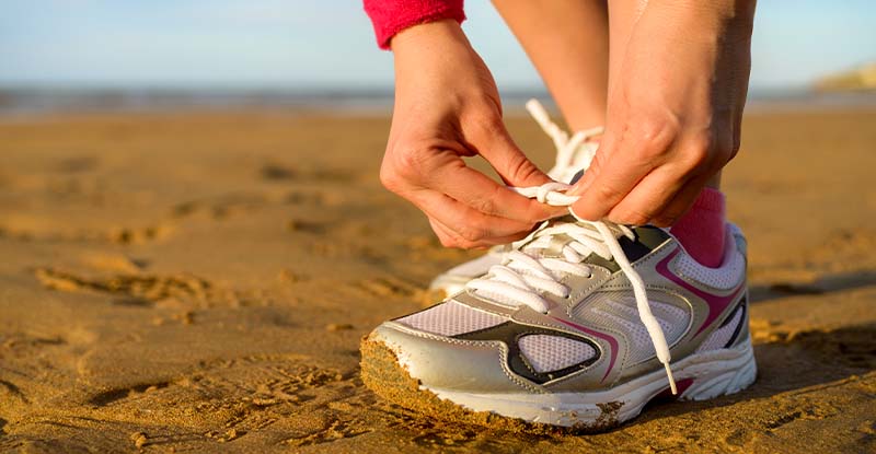 How do I prepare for a CPA preparatory course exam? A photo of a person tying their shoe laces on the beach with the sea and sky in the background.