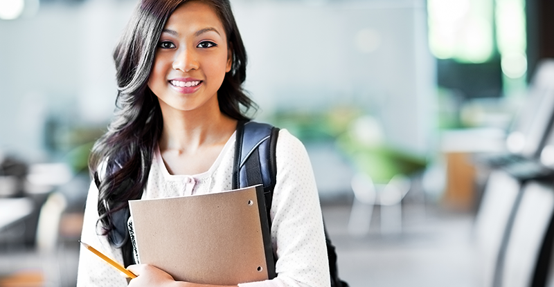 If I’m finishing my degree soon and want to start modules as soon as I can; when should I apply to the program? A photo of a South Asian female student smiling at the camera while carrying a backpack and holding a notebook in her hands.