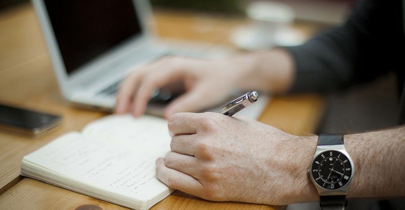 Why am I not granted automatic exemptions on courses taken internationally? A photo of a man writing on a small notebook with a laptop visible in the background.