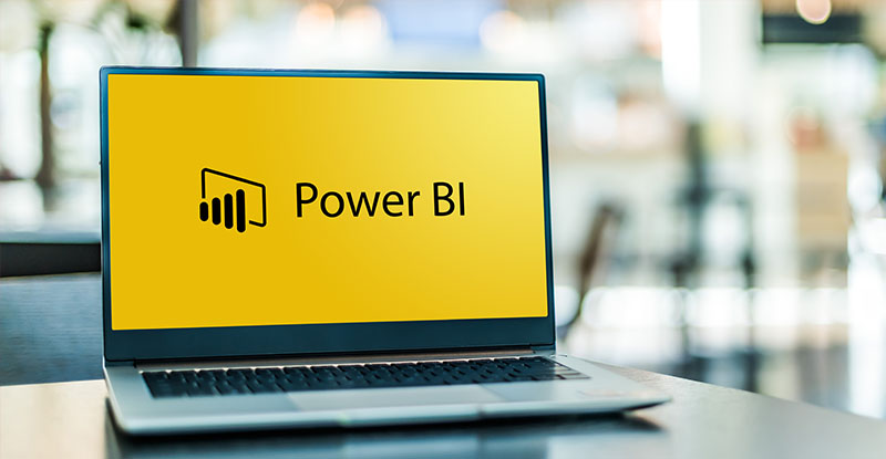 A photo of a laptop open and placed on top of a table and it reads, "Power BI".