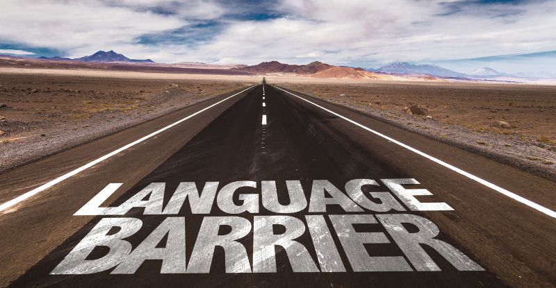 A photo of a long narrow road with mountains in the distance. There is a painted text closer to the bottom of the photo that reads, "Language Barrier".