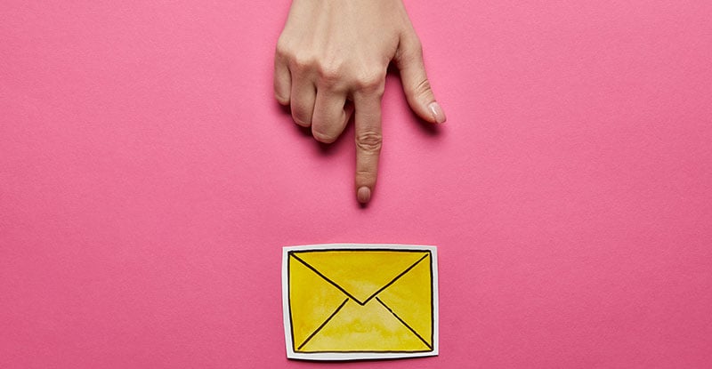 A photo featuring a pink background with a yellow envelope at the bottom and a hand pointing at it from the top.