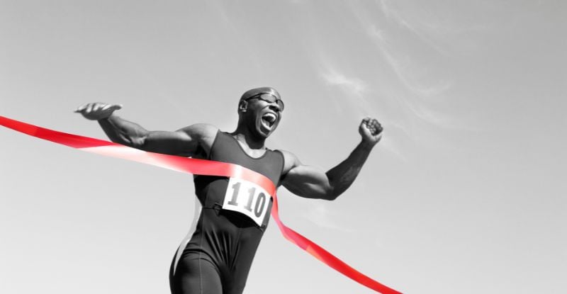 The Arena: Part 2 A black and white photo of an African man winning a race. The ribbon is in red colour.